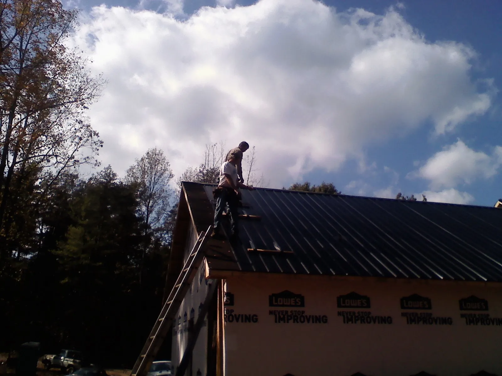 Roofer fastening dark metal panels high against a cloudy sky, from a Roof Inspection job in Goodyear