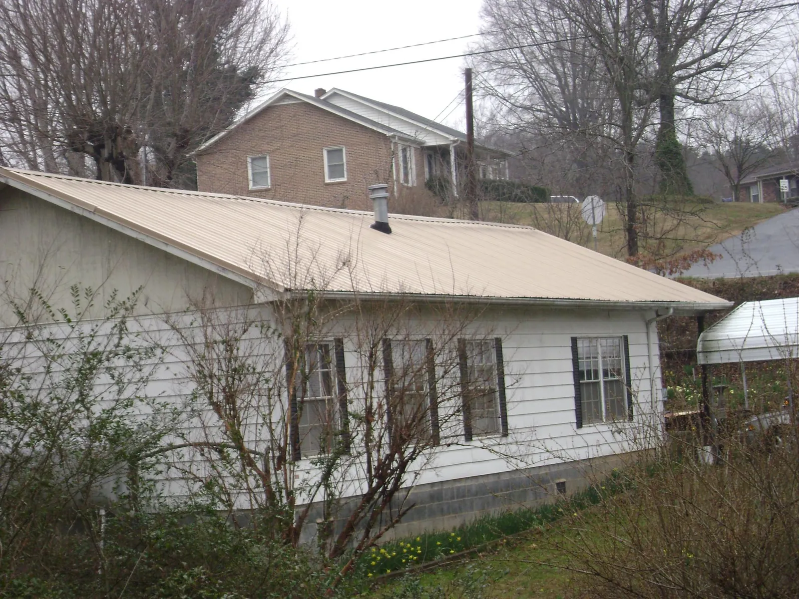 Tan metal roof on a white sided house set into a hillside — Commercial Roofing by Roofing Brothers in Goodyear